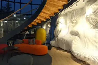 An office lounge with a white sculpted wall, an orange sofa and a spiral staircase overhead