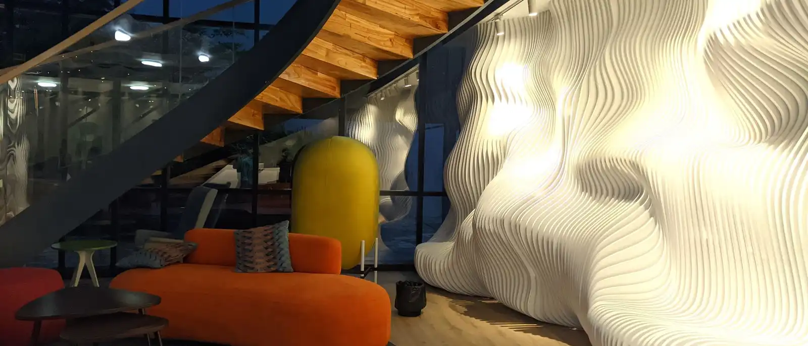 An office lounge with a white sculpted wall, an orange sofa and a spiral staircase overhead