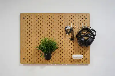 A wooden pegboard on a white wall holding a small plant, headphones and cables
