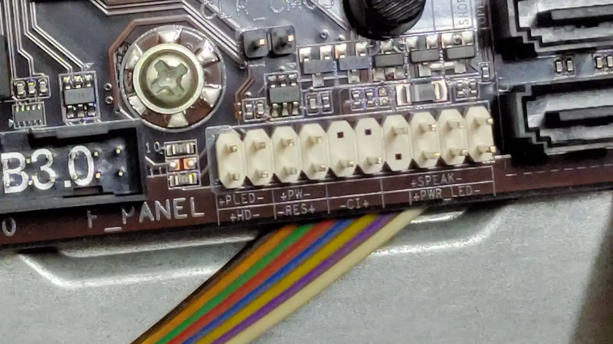 Close-up of the labelled front-panel pins on a computer motherboard with a ribbon cable
