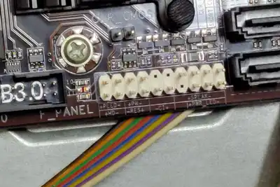 Close-up of the labelled front-panel pins on a computer motherboard with a ribbon cable