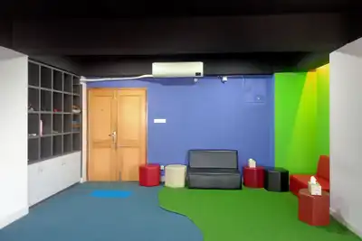 A colourful office corner with a blue wall, green floor, cube shelves and small red stools