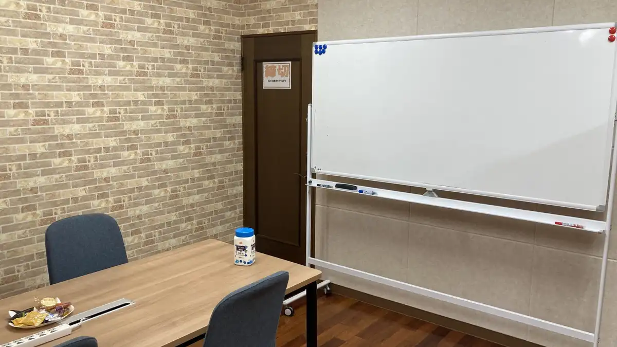 A small meeting room with a wooden table, grey chairs and a blank whiteboard on wheels