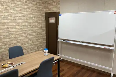A small meeting room with a wooden table, grey chairs and a blank whiteboard on wheels