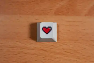 A single grey keycap printed with a red pixel heart on a wooden table