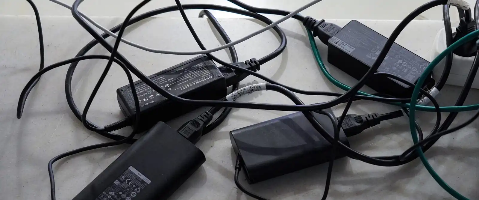 A tangle of black power adapters and cables on a pale stone surface
