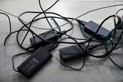 A tangle of black power adapters and cables on a pale stone surface