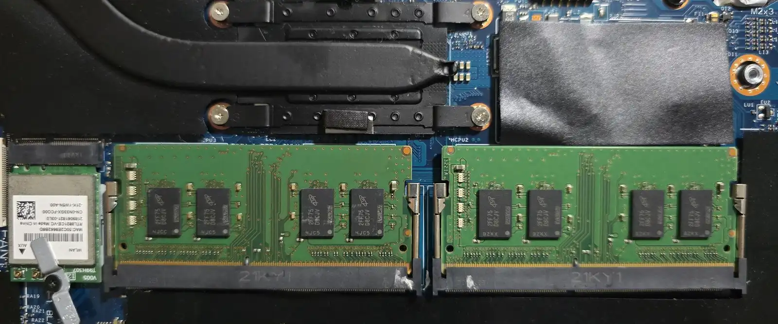 Two memory modules installed on an open laptop motherboard next to its cooling pipes