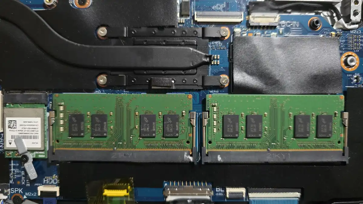 Two memory modules installed on an open laptop motherboard next to its cooling pipes