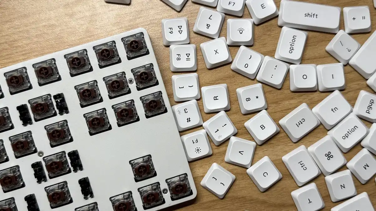 A white low-profile keyboard with its keycaps pulled off and scattered across a wooden table