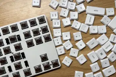 A white low-profile keyboard with its keycaps pulled off and scattered across a wooden table