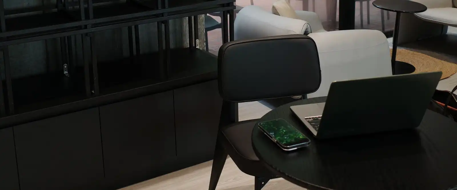 A laptop on a round black table beside a black armchair in a dark, minimal showroom
