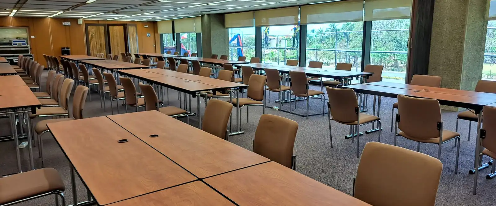 A large training room with long rows of wooden tables and chairs facing a window wall