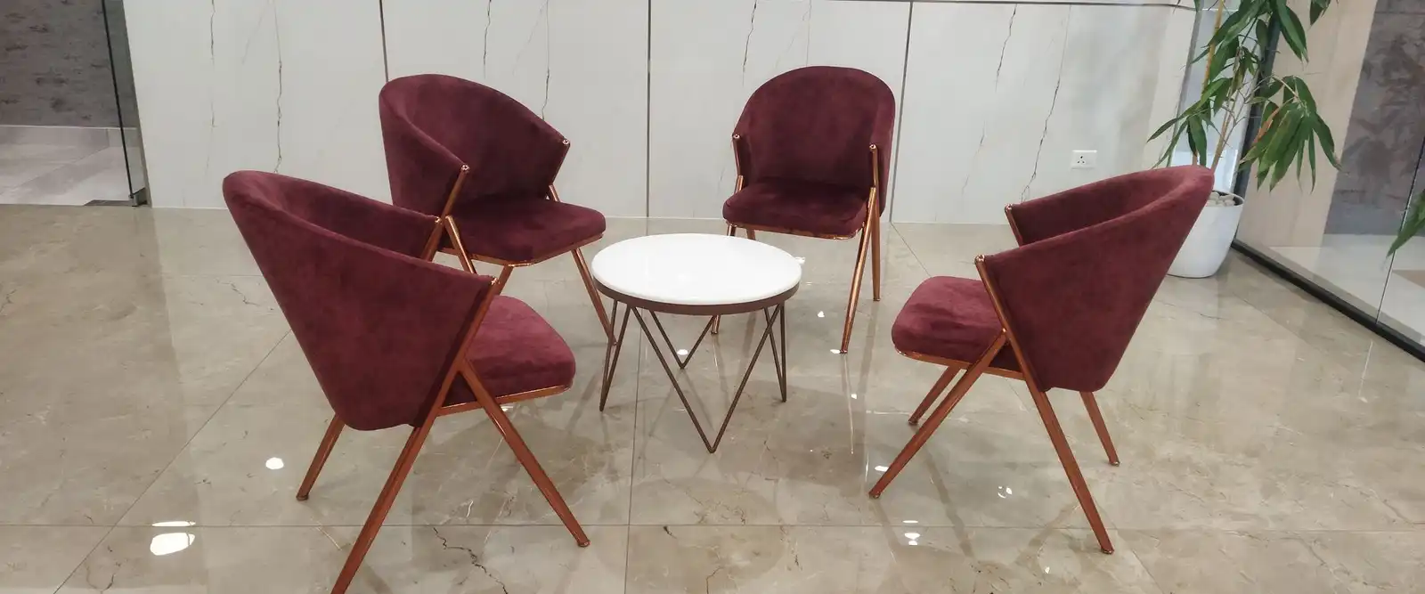Four burgundy armchairs around a small white table in a bright lobby with a marble floor